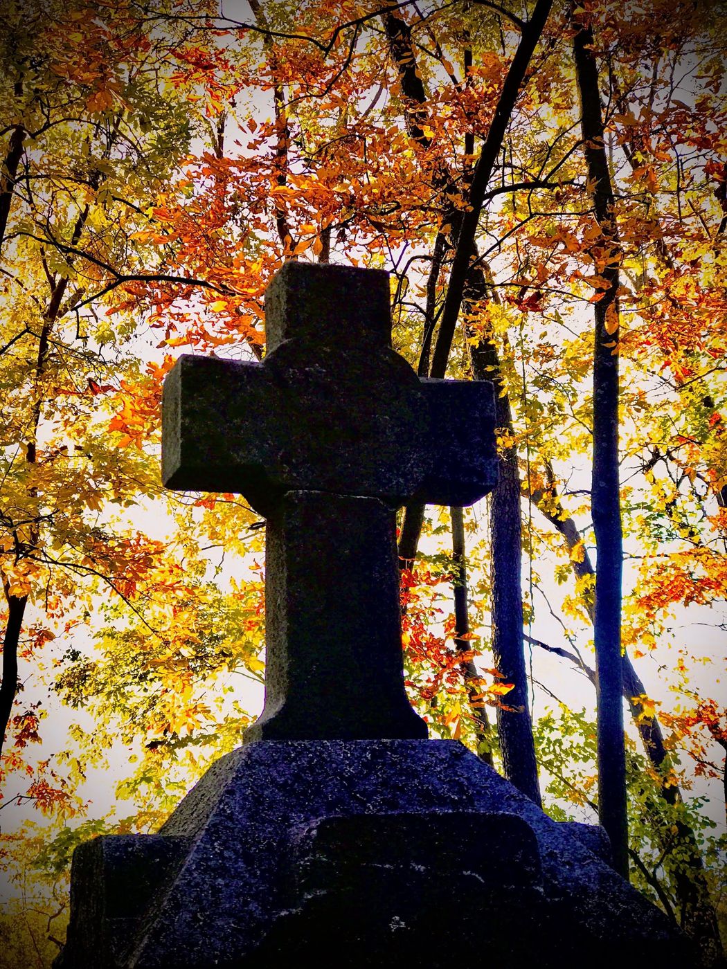 A carved stone cross framed by autumn leaves at Kessler Cemetery