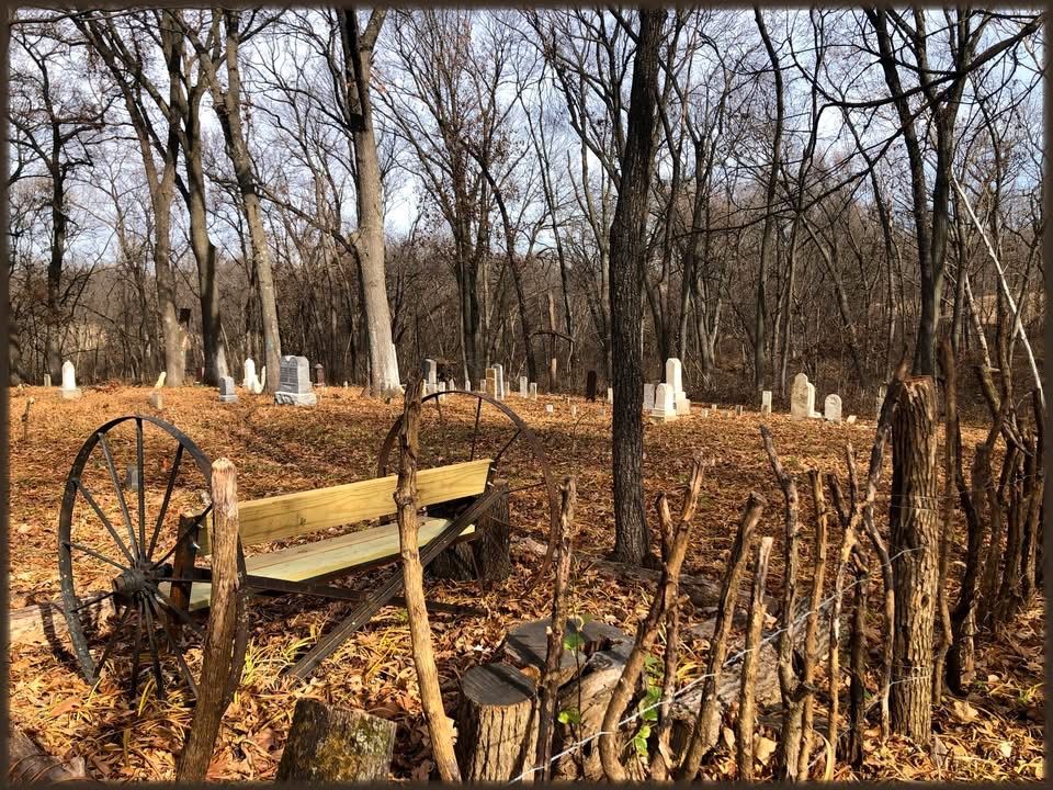 Old wagon wheels and a wooden cart among the trees, with headstones in the background